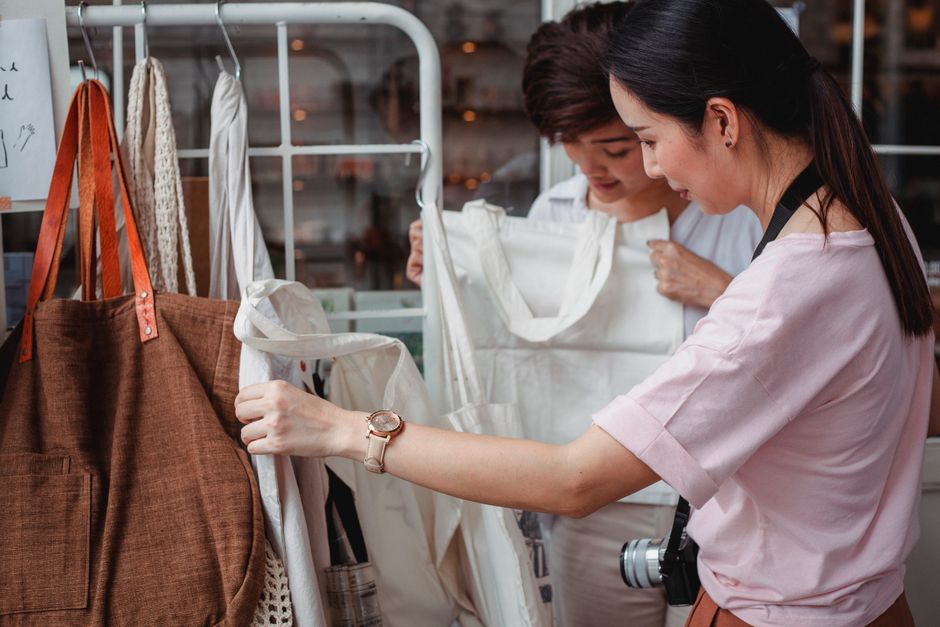 Side view of fashionable young ethnic female friends choosing stylish eco friendly cotton bags in boutique