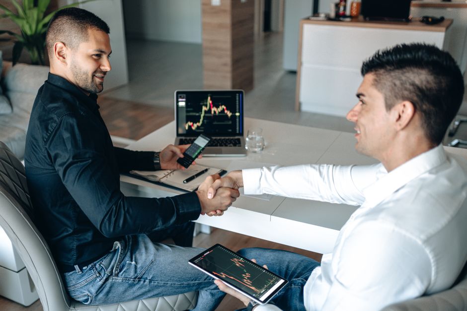 Two businessmen shake hands over a successful stock trading agreement using technology in a modern office.